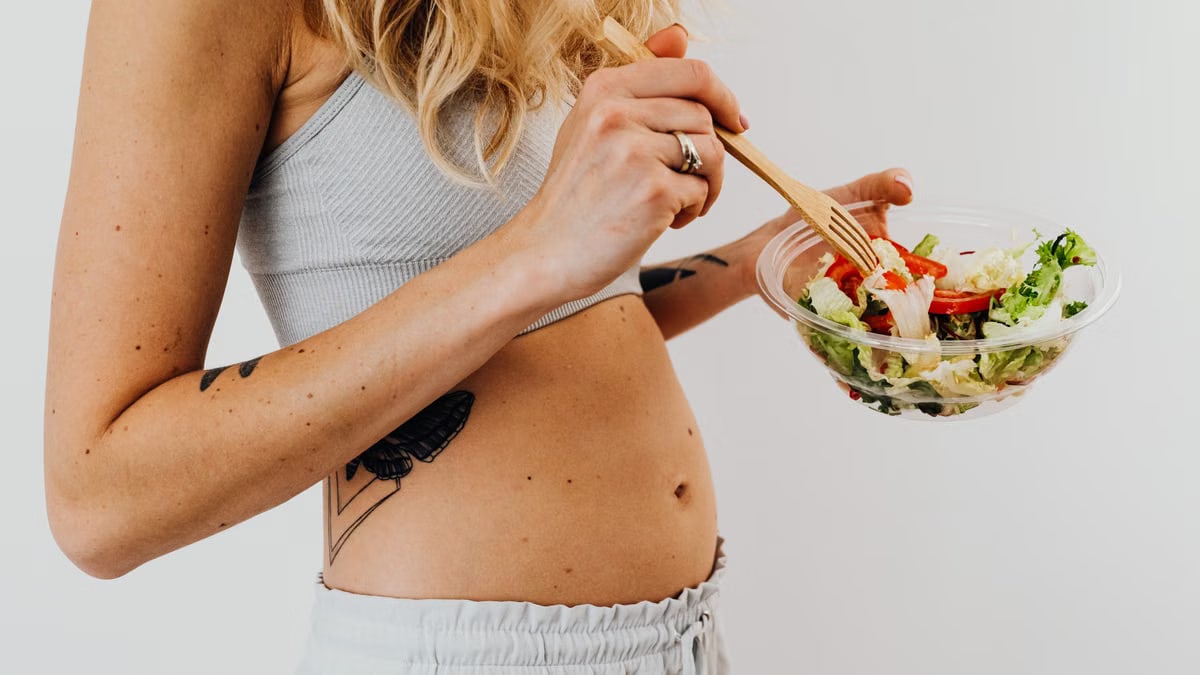 Close-up of a woman in a crop top enjoying a fresh salad indoors.